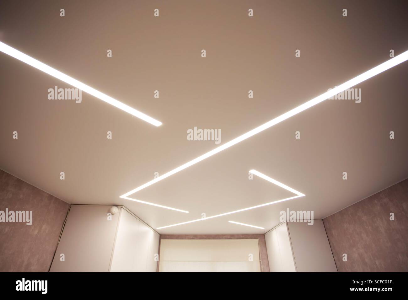 Soffitto allungato di design moderno con linee LED illuminate in camera. Foto Stock