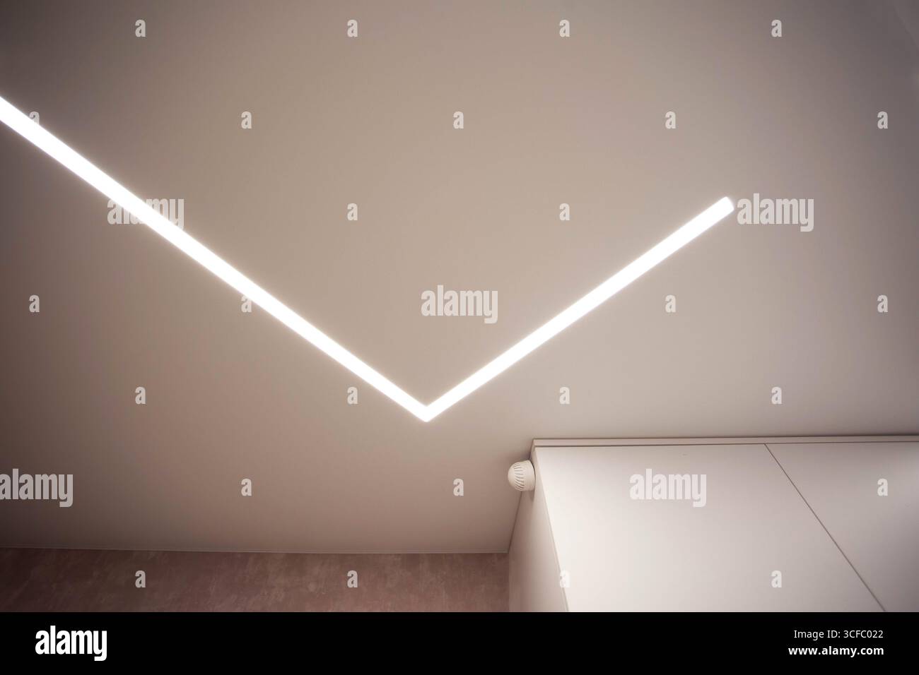 Soffitto allungato di design moderno con linee LED illuminate in camera. Foto Stock