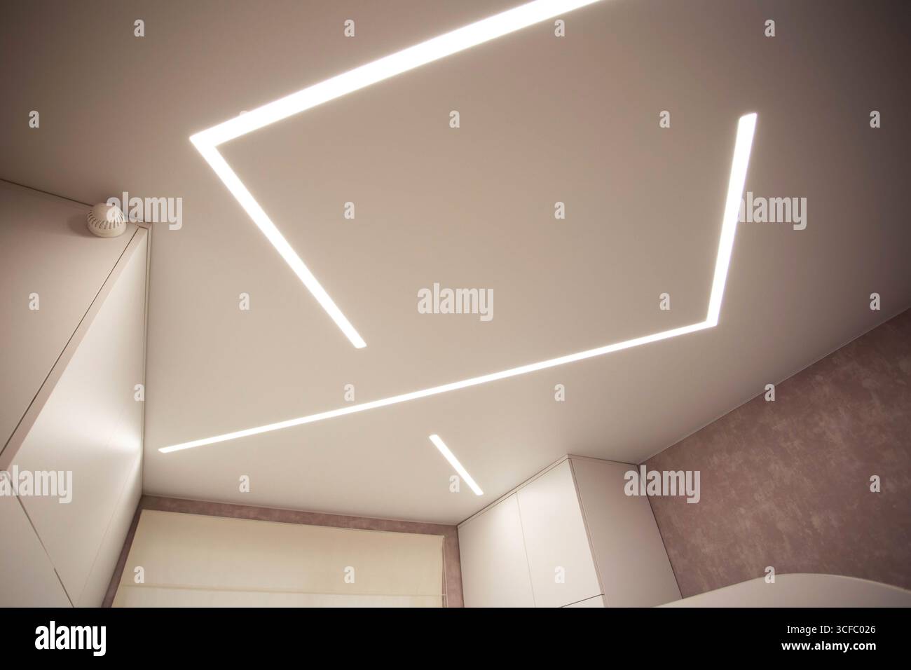 Soffitto allungato di design moderno con linee LED illuminate in camera. Foto Stock