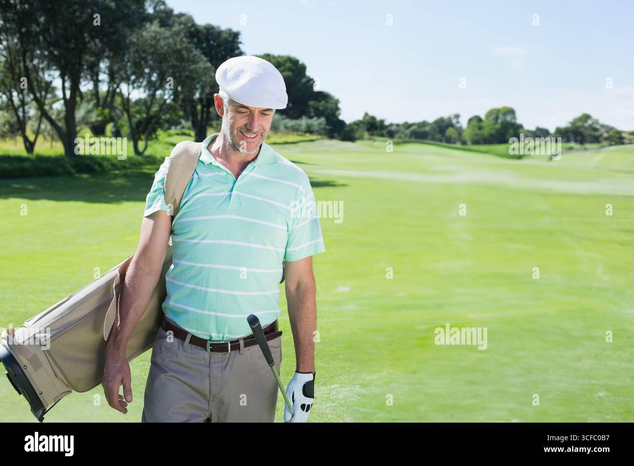 Golfista di mezza età che cammina sul fairway indossando una polo a righe con borsa da golf e spazio fotocopie Foto Stock