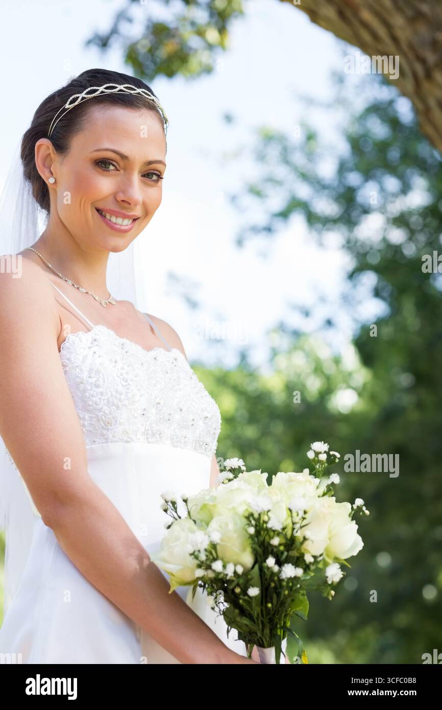 Donna sorridente, con bouquet di rose bianche in giardino con abito da sposa e velo, copia spazio Foto Stock