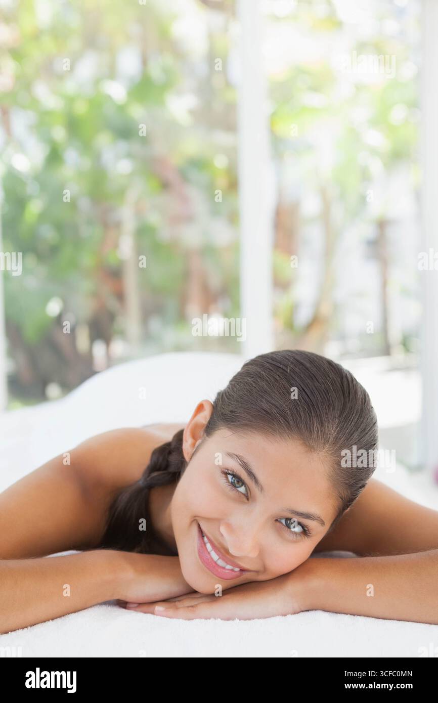 Donna asiatica sdraiata a faccia in giù sul tavolo da massaggio nella sala spa con pannelli di vetro e asciugamano Foto Stock