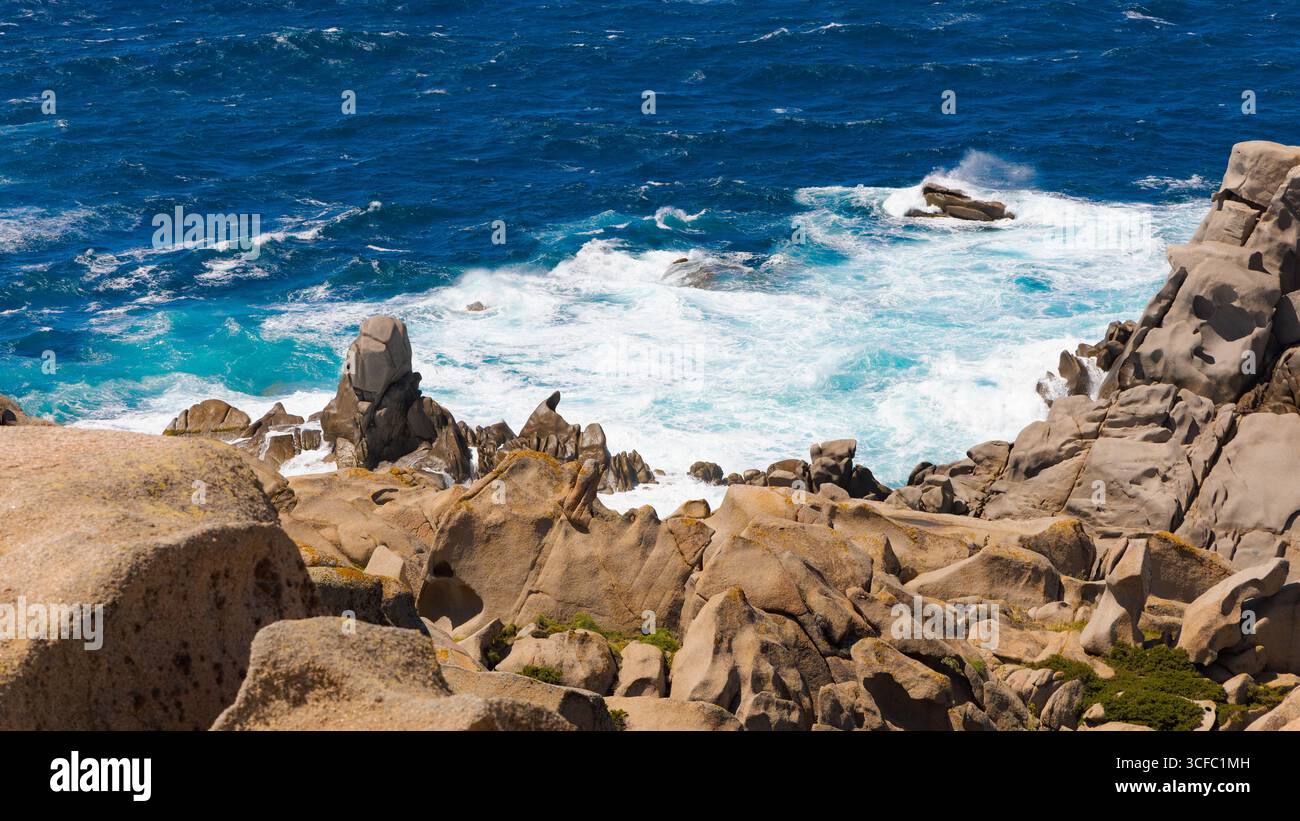 Le onde che si infrangono colpiscono rocce di granito scolpite a Capo testa, in Sardegna, con acque turchesi, spruzzi di mare e aspre formazioni costiere sotto il sole estivo. Foto Stock