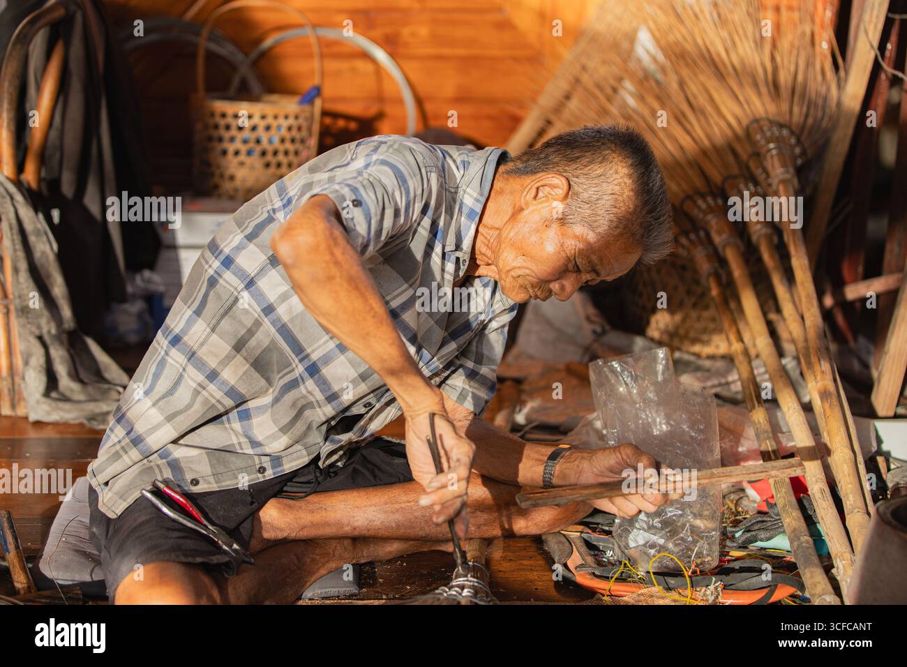 Vecchio artigiano thailandese che produce scopa con foglie di cocco al crepuscolo Foto Stock