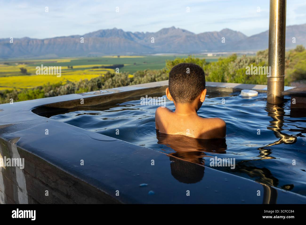 Ragazzo in una vasca idromassaggio con vista sulle montagne Foto Stock