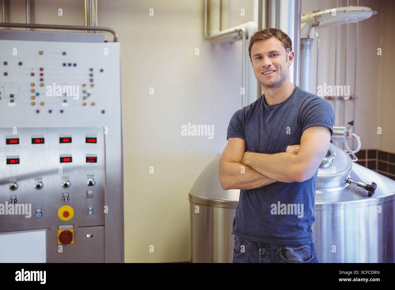 Il tecnico si trova accanto al serbatoio di fermentazione in acciaio inox e al pannello di controllo nella sala birreria Foto Stock