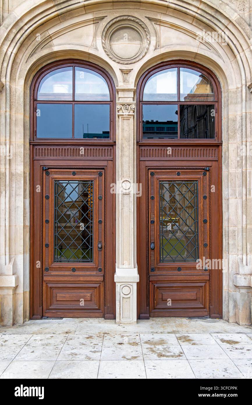 Porte doppie ornate in legno con finestre ad arco. Primo piano di eleganti doppie porte in legno con finestre a reticolo in ferro decorativo e pannelli in vetro ad arco Foto Stock