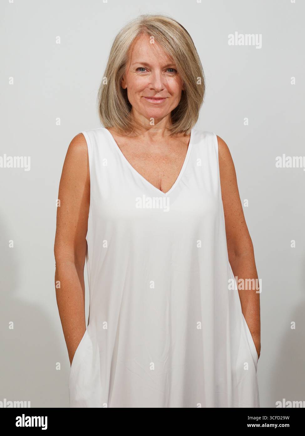 Donna sorridente con capelli a spalla in un abito bianco senza maniche su sfondo semplice. Italia Foto Stock Donna sorridente con capelli a spalla in un abito bianco senza maniche su sfondo semplice. Italia Foto Stock