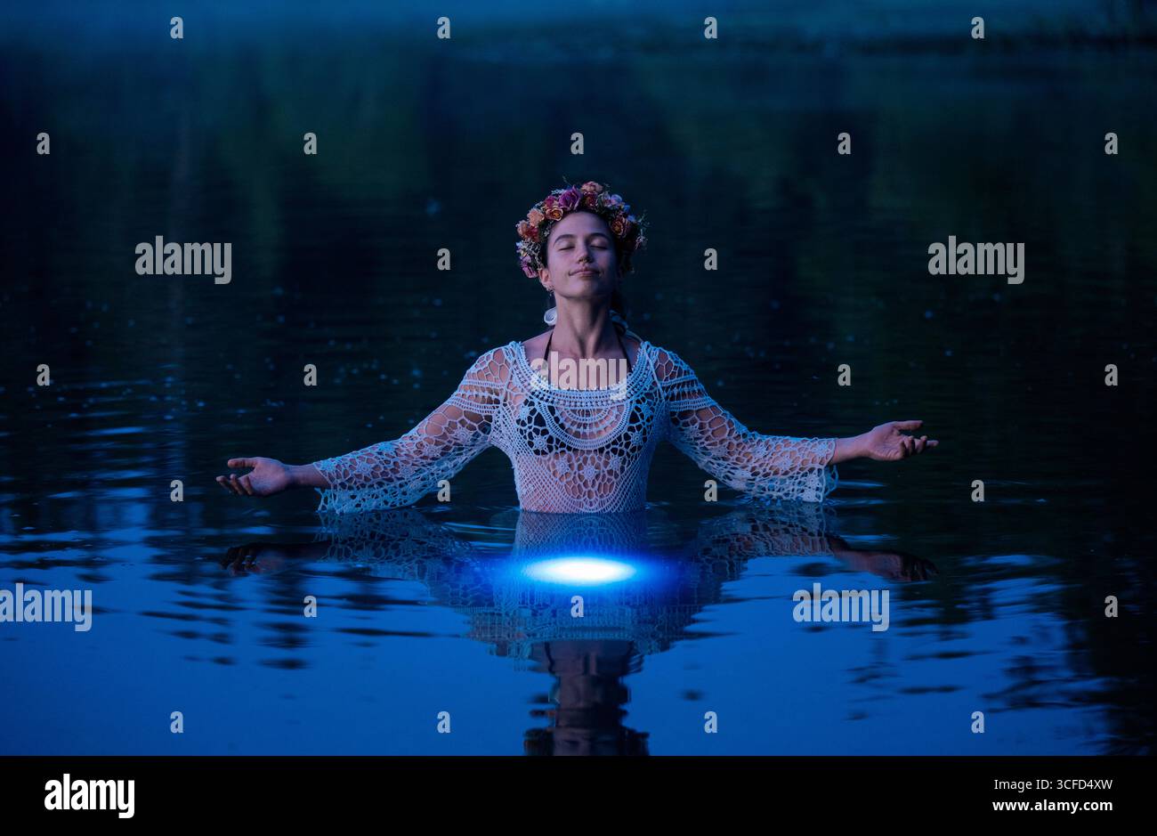 Donna in piedi in acque calme che indossa un abito all'uncinetto e una corona floreale con le braccia allungate. WASHINGTON, STATI UNITI Foto Stock