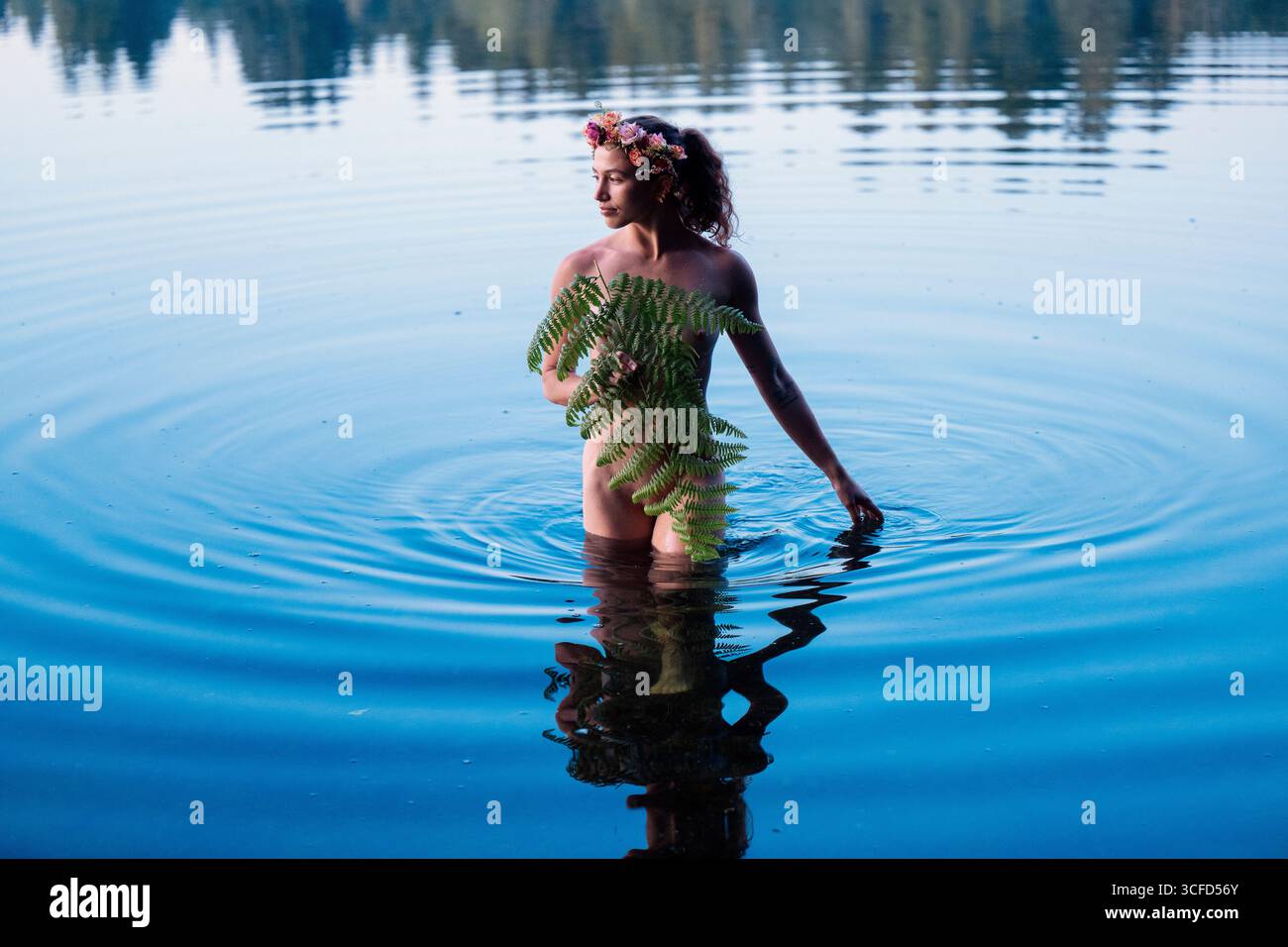 Donna con una corona floreale parzialmente sott'acqua che regge una felce, circondata da un lago sereno. WASHINGTON, STATI UNITI Foto Stock