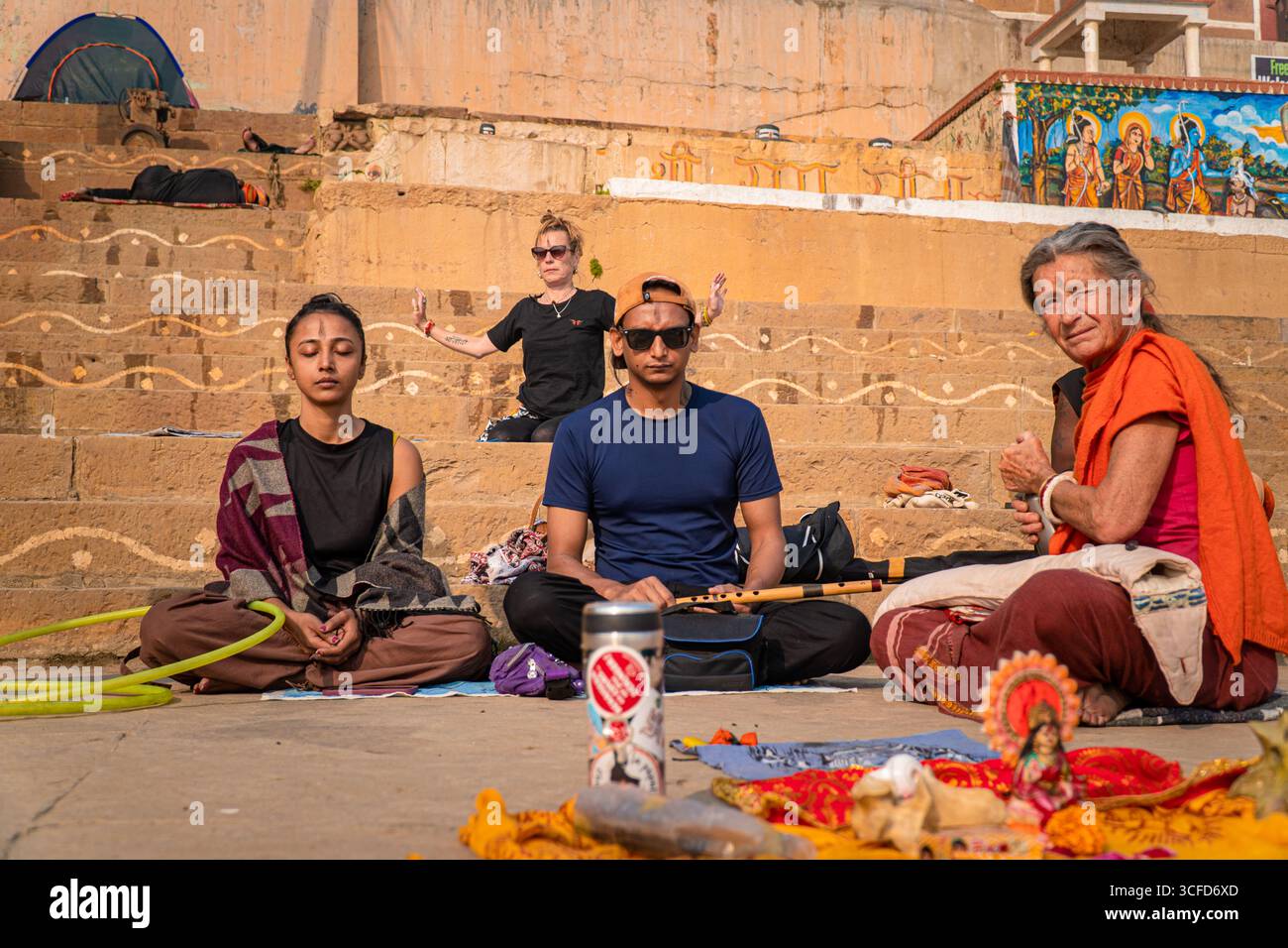 Gruppo variegato di locali e turisti che meditano e adorano i Ghati del fiume Gange a Varanasi, India. Foto Stock