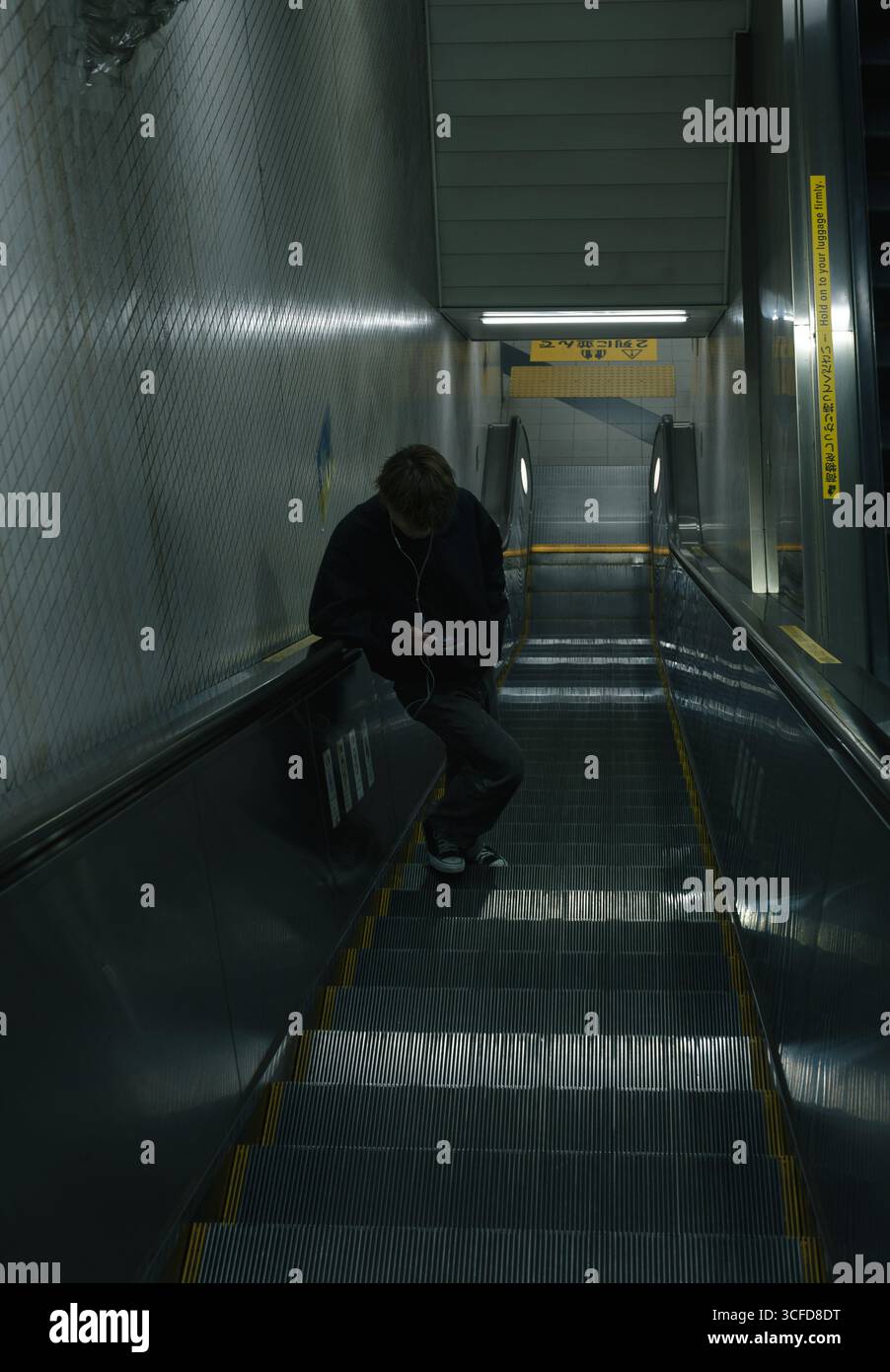 Il pendolare di Lonesome corre su una scala mobile della metropolitana di Kyoto, indossa cuffie e telefono in mano Foto Stock