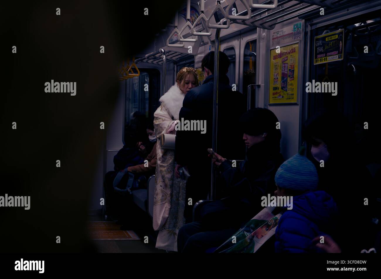 La carrozza della metropolitana di Kyoto, una giovane donna in un kimono ornato, si distingue contro la folla di pendolari poco illuminata Foto Stock