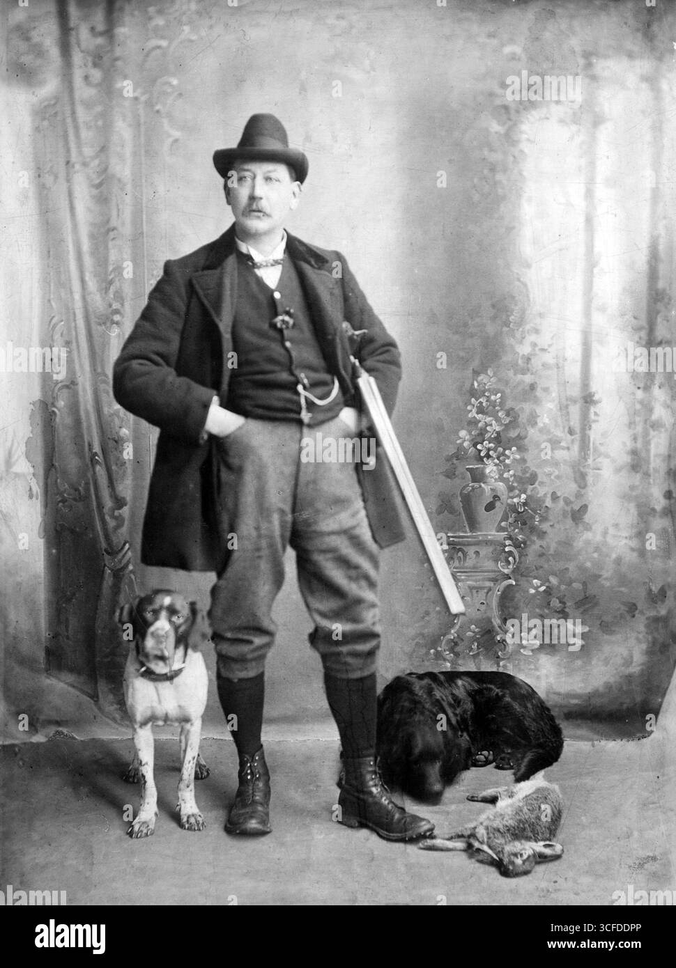 Uomo, forse un guardiano, che posa con il suo fucile, cani e una lepre morta Foto Stock