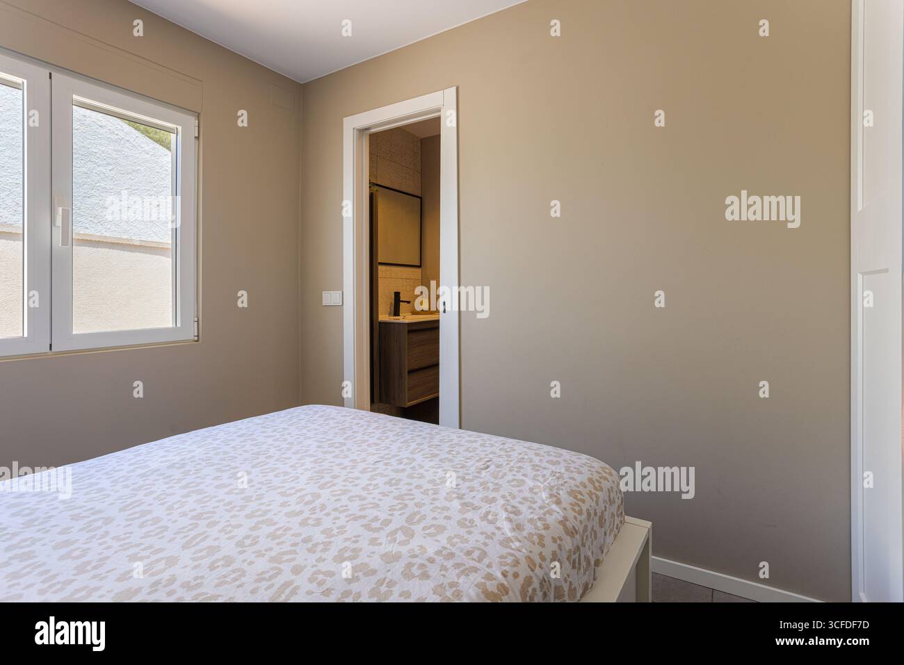 Camera con letto doppio, pareti beige e vista sul bagno privato. Foto Stock