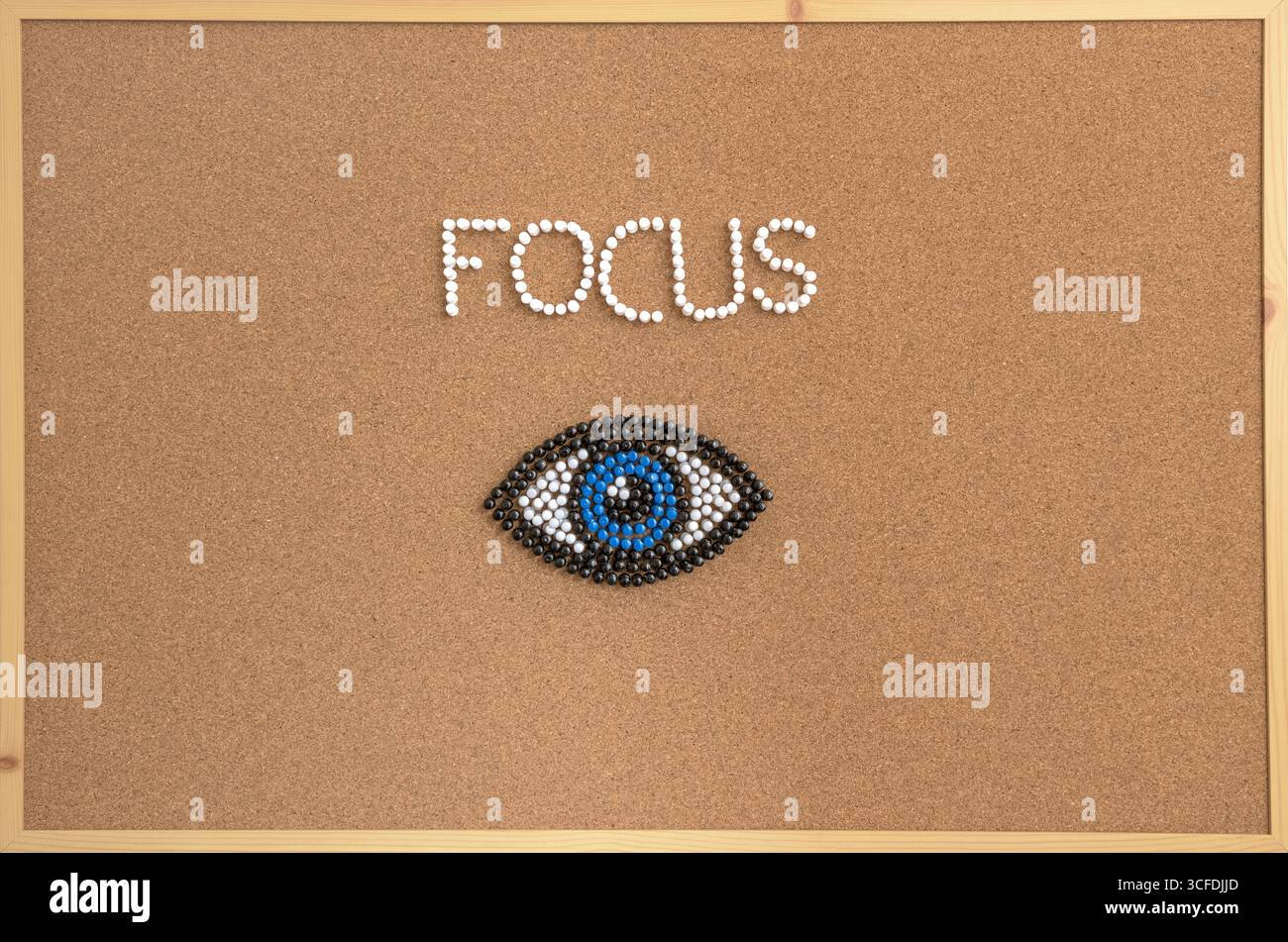 Immagine concettuale creativa della parola "MESSA A FUOCO" e simbolo di un occhio disposto con perni colorati su una bacheca in sughero. Foto Stock