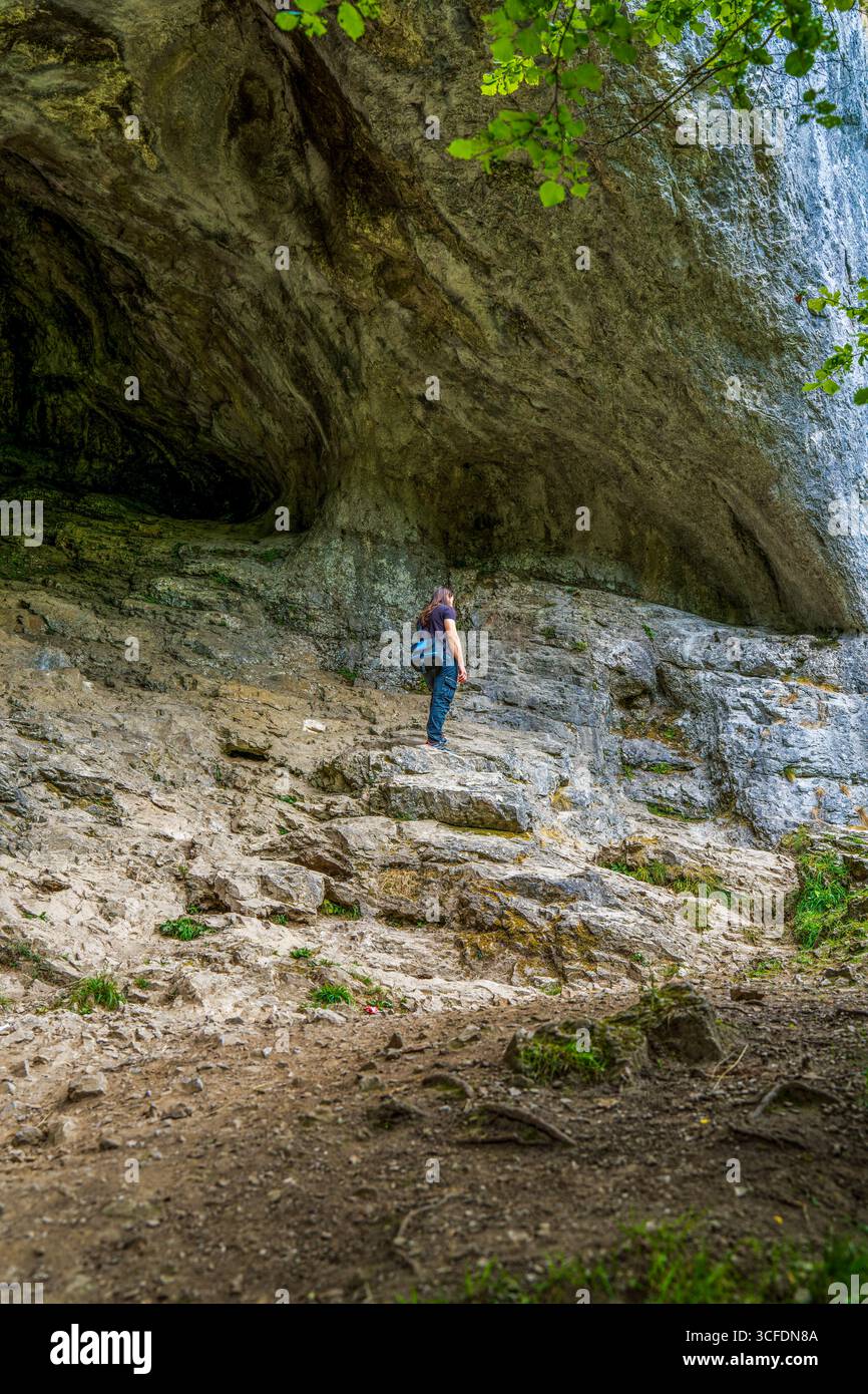 Esplorando gli ingressi della Majestic Cave di Dovedale nel Peak District, Un escursionista che si erge contro torreggianti formazioni rocciose di calcare Foto Stock Esplorando gli ingressi della Majestic Cave di Dovedale nel Peak District, Un escursionista che si erge contro torreggianti formazioni rocciose di calcare Foto Stock