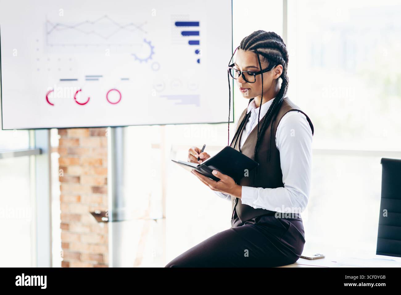 Donna d'affari professionista che prende appunti durante una presentazione strategica in un ufficio moderno con analisi dei dati Foto Stock