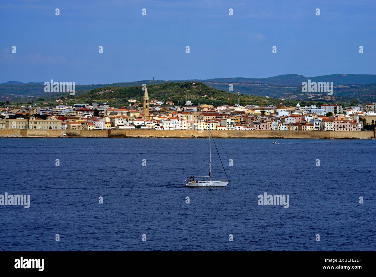 Lo yacht "Indy" naviga nel porto di Alghero in Sardegna. Sullo sfondo si vedono le mura marittime e parte della città. Foto Stock