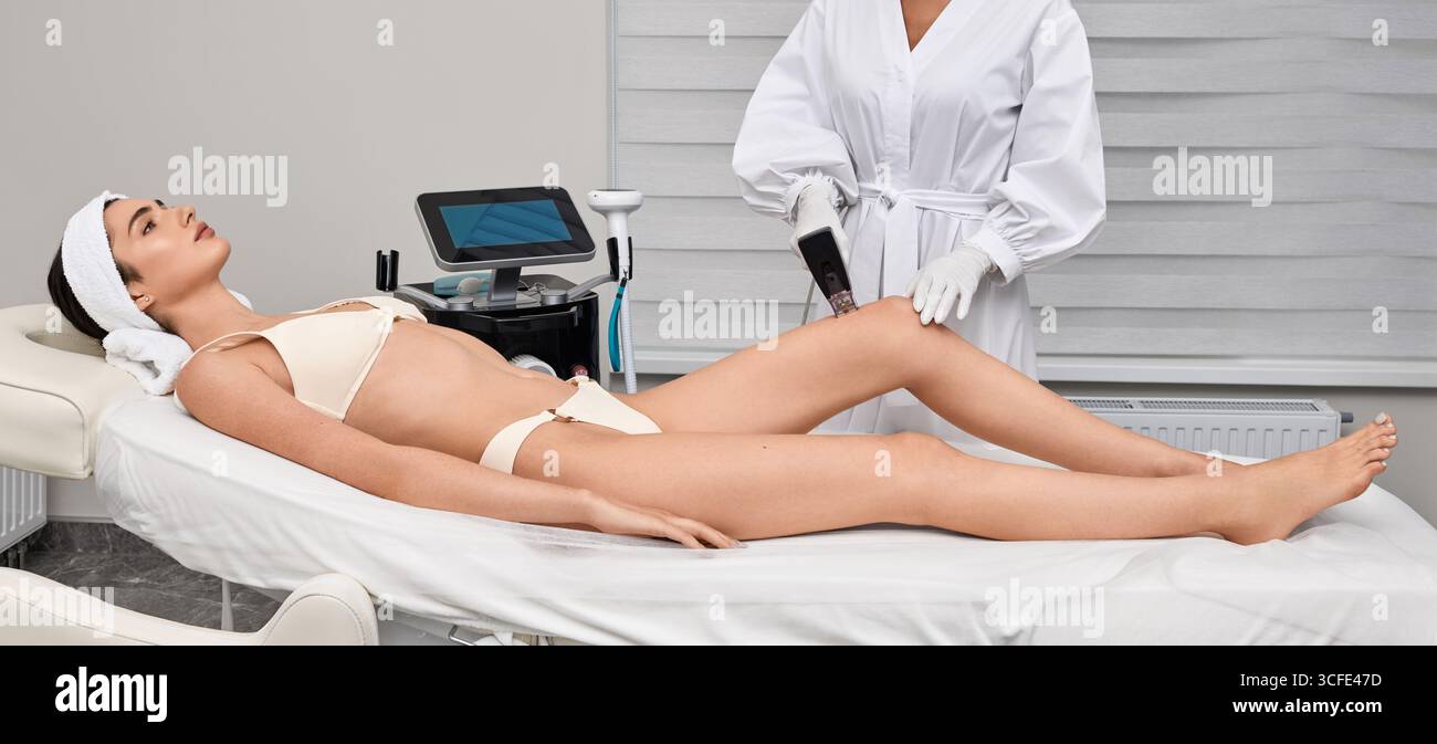 Lunghe gambe femminili durante la procedura di sollevamento della pelle a radiofrequenza con estetista in salone termale. Sollevamento RF della pelle delle gambe Foto Stock