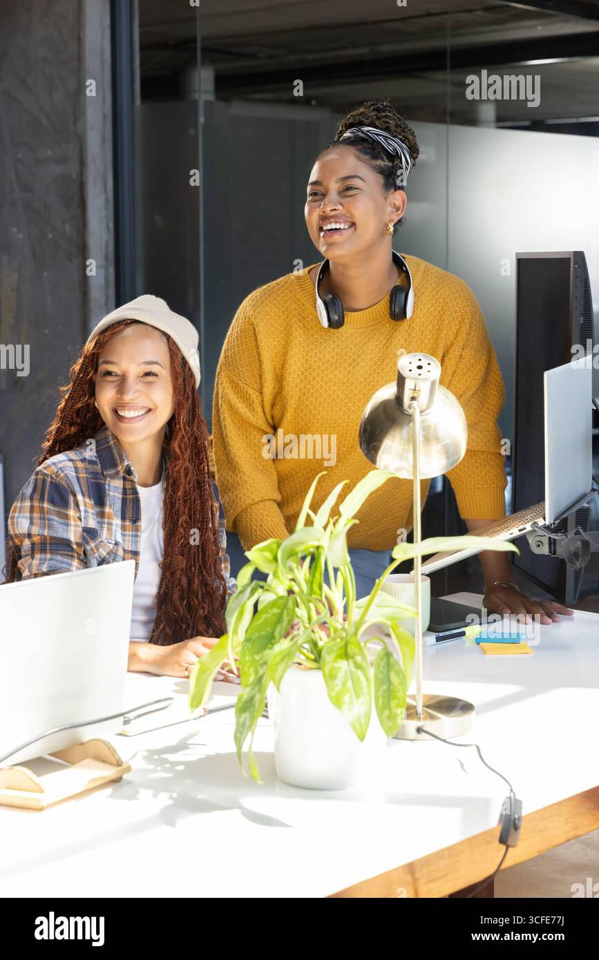 Diverse collaboratrici che collaborano con un computer portatile e utilizzano appunti vicino allo stabilimento in ufficio Foto Stock