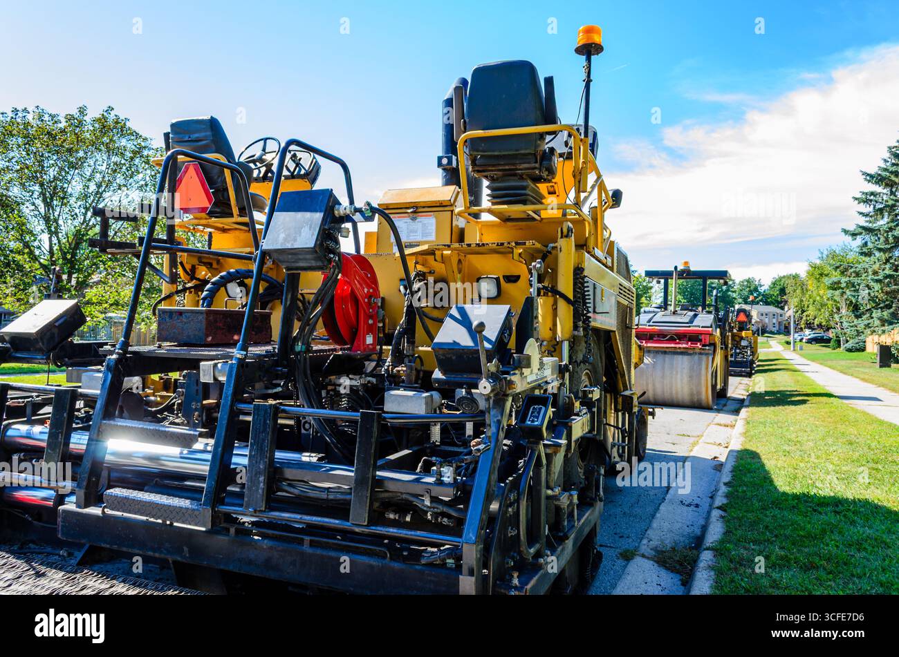 Vista posteriore di un'asfaltatrice stradale e di una serie di attrezzature da costruzione su una strada residenziale in un giorno d'estate Foto Stock