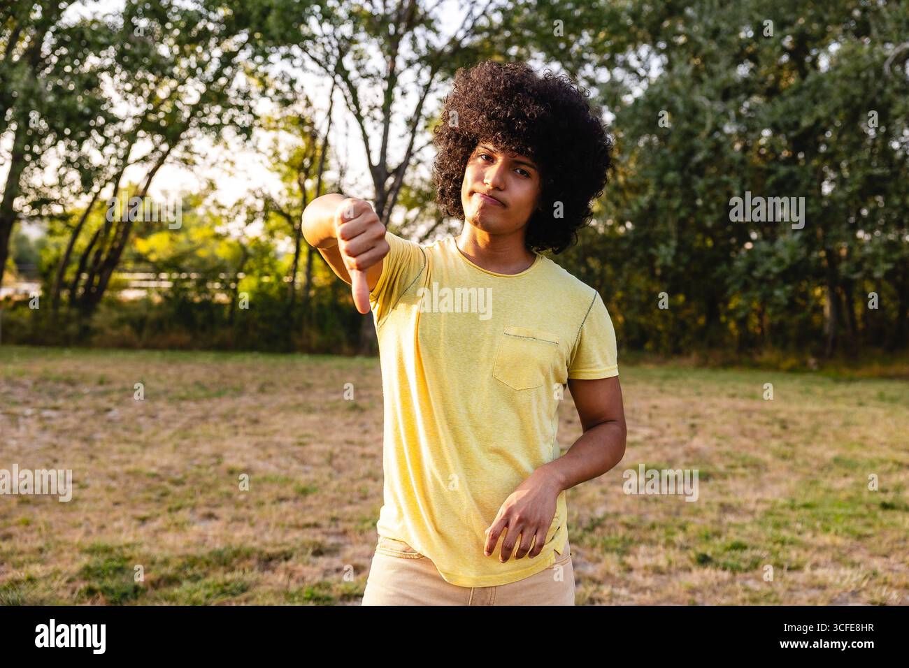 Un giovane che mostra un gesto con i pollici in un parco che esprime disapprovazione Foto Stock