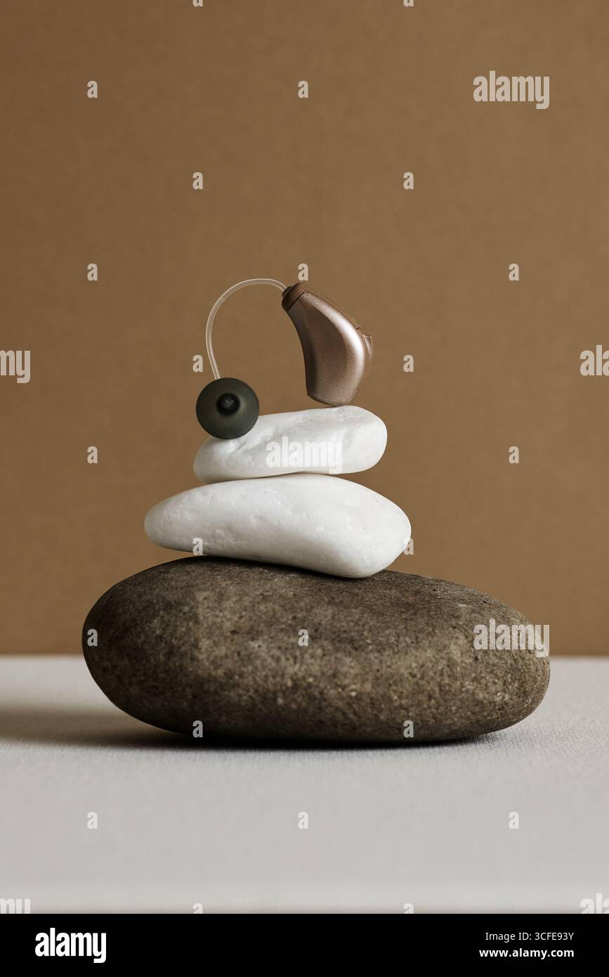 L'apparecchio acustico dietro l'orecchio si bilancia delicatamente su pietre impilate, creando un senso di pace ed equilibrio. Audiologia Foto Stock