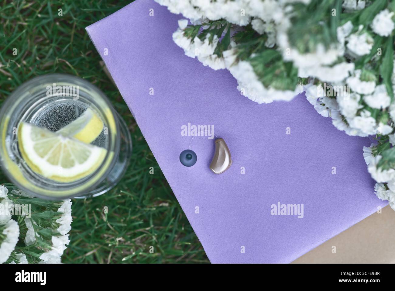 Apparecchio acustico beige in periwinkle con limonata, fiori. La tranquillità della natura diurna offre un buon umore all'utente con soluzioni per l'udito Foto Stock