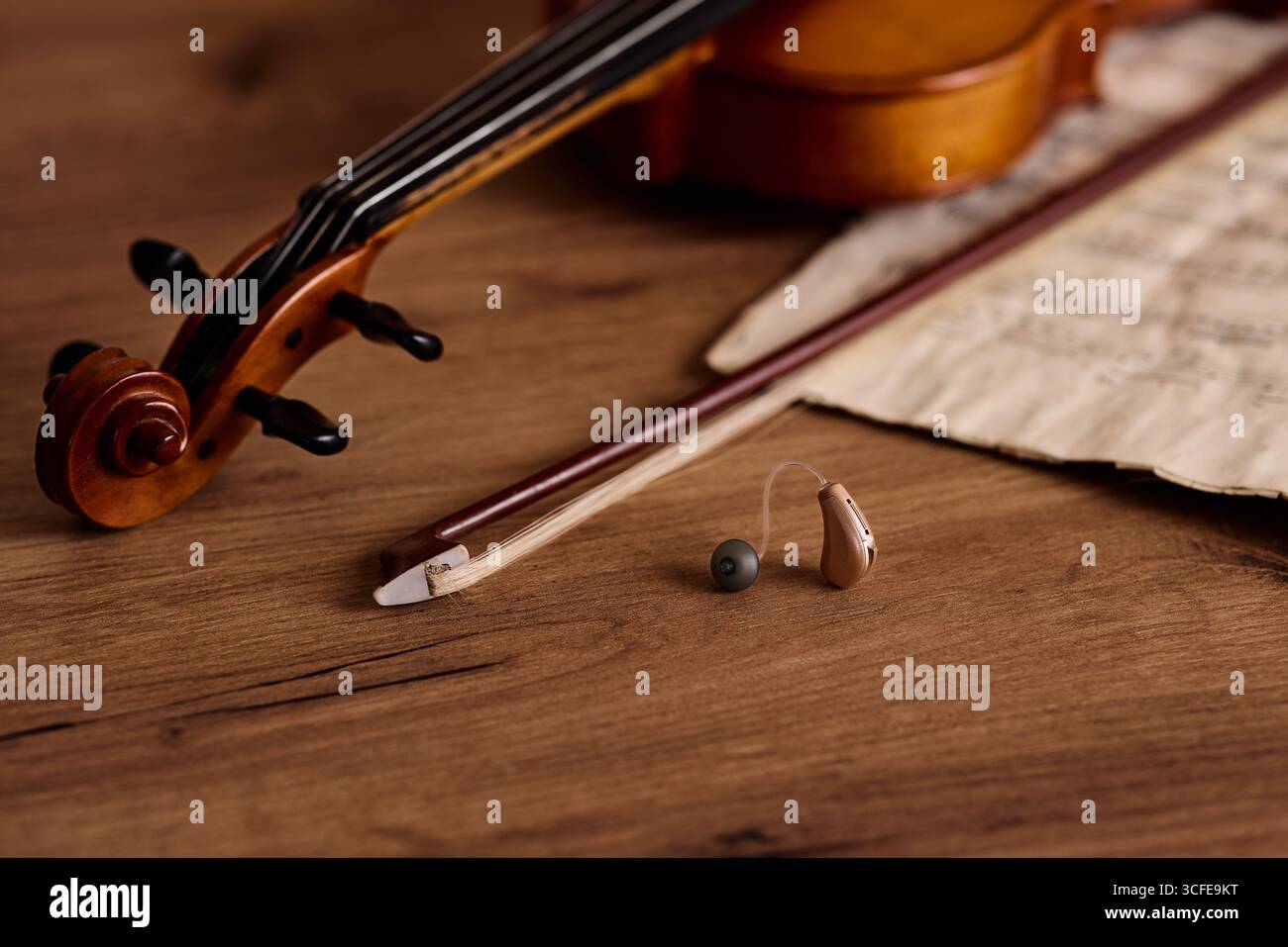 Apparecchio acustico BTE accanto a un violino e arco su legno, mettendo in evidenza soluzioni uditive per gli amanti della musica Foto Stock