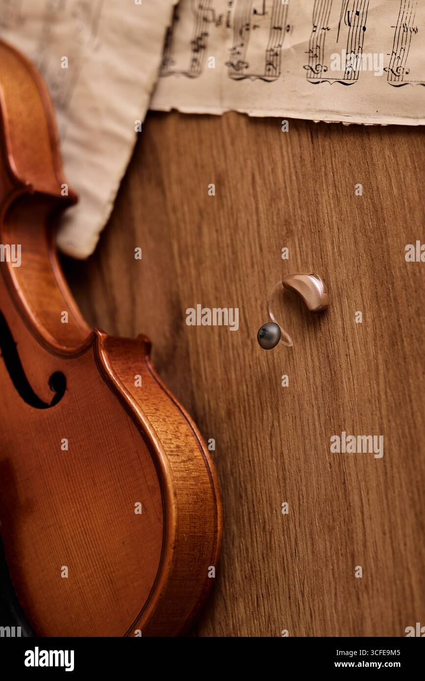Un delicato apparecchio acustico si appoggia accanto al violino, unendo innovazione uditiva e abilità artistica in un accogliente studio. Soluzioni per l'udito, concetto Foto Stock