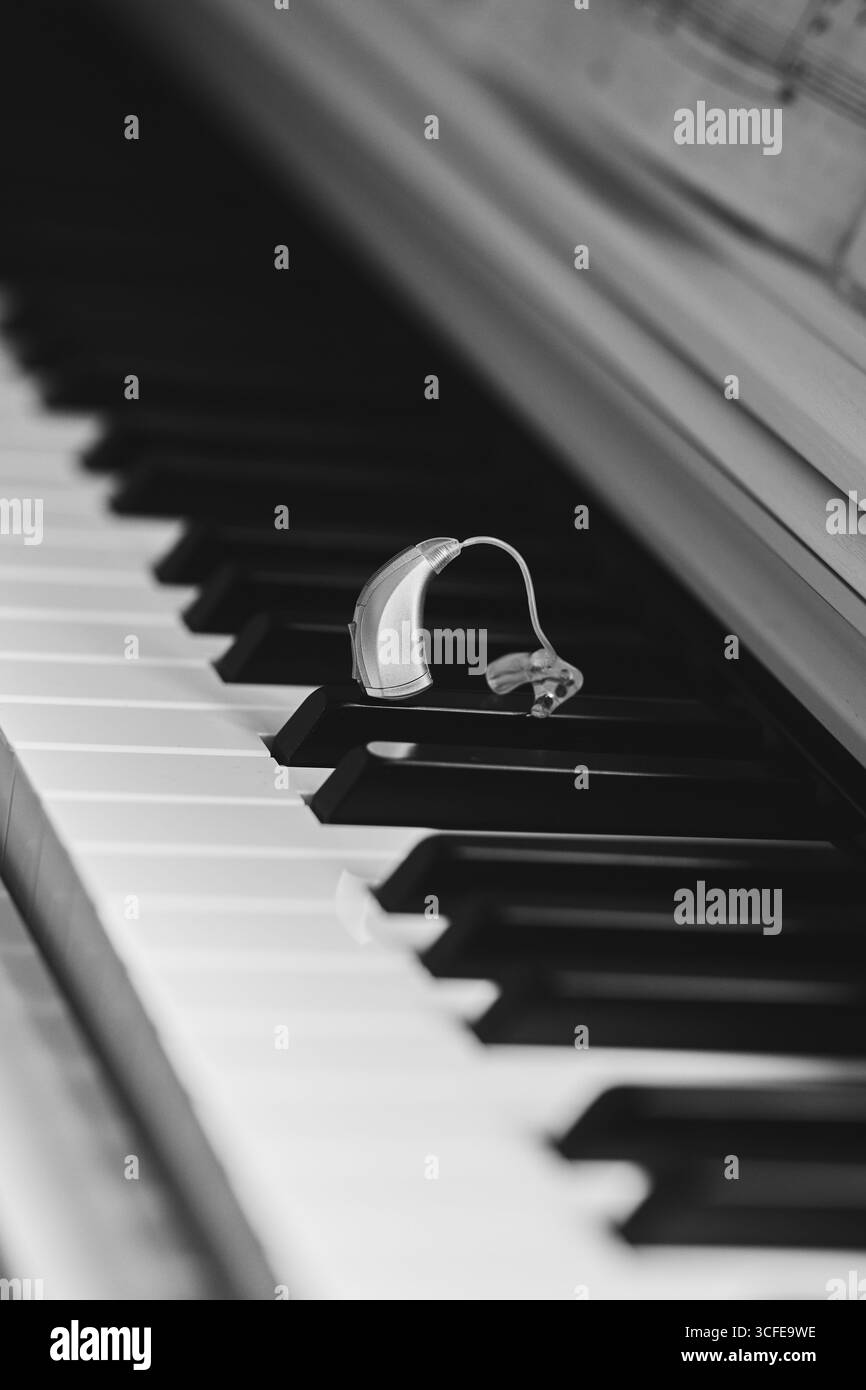 Soluzioni per l'udito. L'apparecchio acustico poggia sui tasti del pianoforte, simboleggiando la combinazione di musica e accessibilità sonora Foto Stock