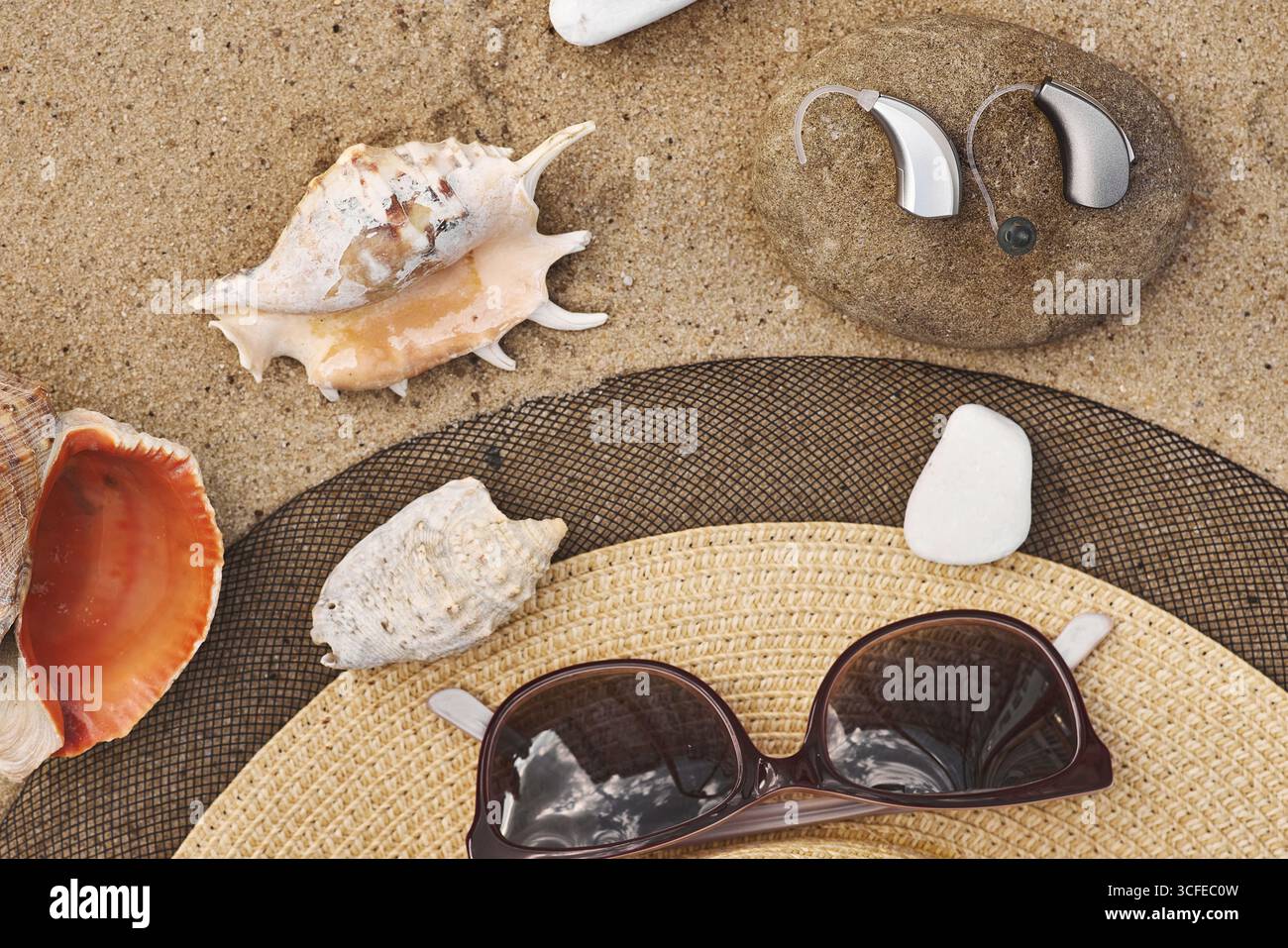Apparecchi acustici annidati tra conchiglie e occhiali da sole, che combinano soluzioni per la salute con le vacanze. Soluzioni per l'udito per tutti i giorni Foto Stock
