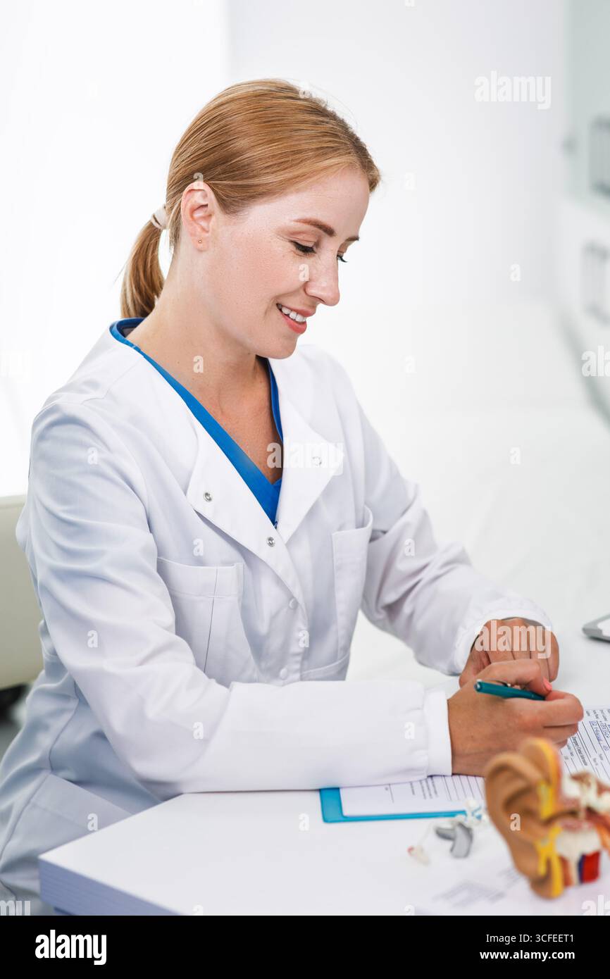 Consulenza audiologa, trattamento della sordità. Medico udente seduto nel suo ufficio di audiologia durante la sua consultazione Foto Stock