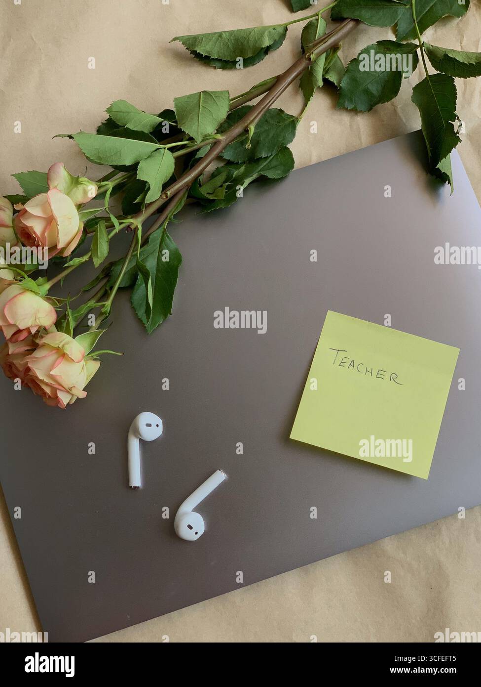 Computer portatile, auricolari e fiori, vista dall'alto, spazio fotocopie. Ambiente di lavoro moderno. Nota adesiva con un insegnante di parole scritto a mano. Area di lavoro. - Immagine stock catturata con smartphone