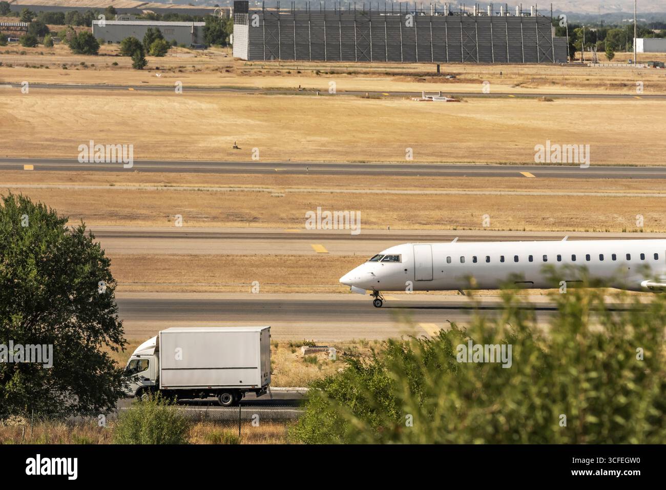 Business jet che attraversa una pista secondaria con un perfetto riflesso in una pozza di pioggia recente Foto Stock