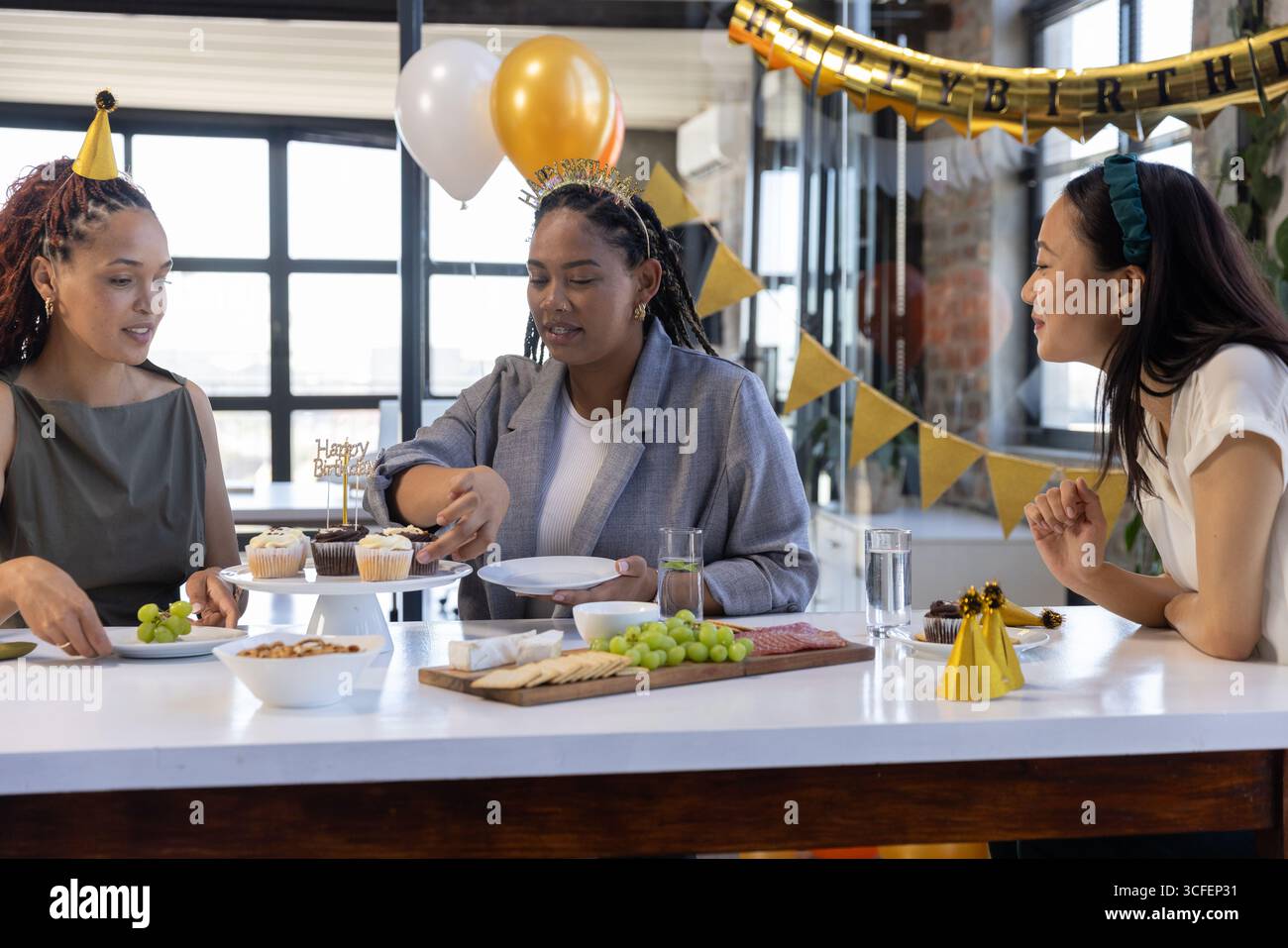 Diverse amiche che festeggiano il compleanno a Kitchen Island con cupcake e tagliere di salumi Foto Stock