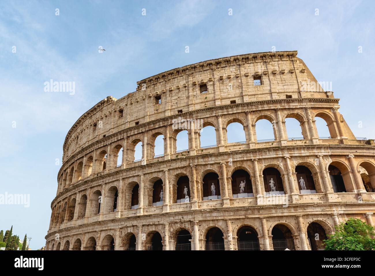 Il Colosseo di Roma, in Italia, iconico anfiteatro antico con file di archi e facciata in pietra illuminata dal sole sotto il cielo blu Foto Stock