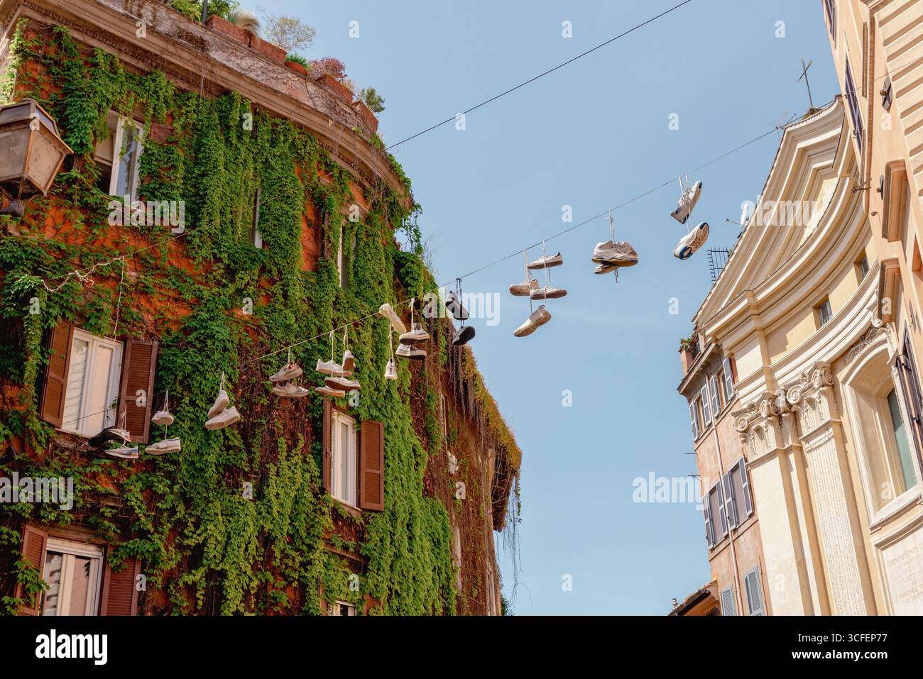 Stravagante scena di strada a Roma, in Italia, con sneakers appese a un filo tra edifici storici, una ricoperta di edera verde Foto Stock Stravagante scena di strada a Roma, in Italia, con sneakers appese a un filo tra edifici storici, una ricoperta di edera verde Foto Stock