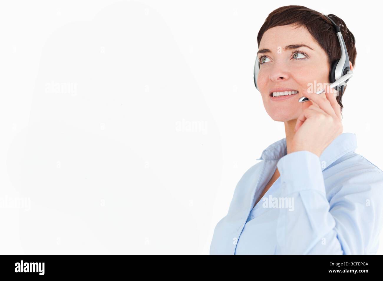 Rappresentante del servizio clienti donna che inclina la testa e sorride con le cuffie in ufficio, spazio per le copie Foto Stock