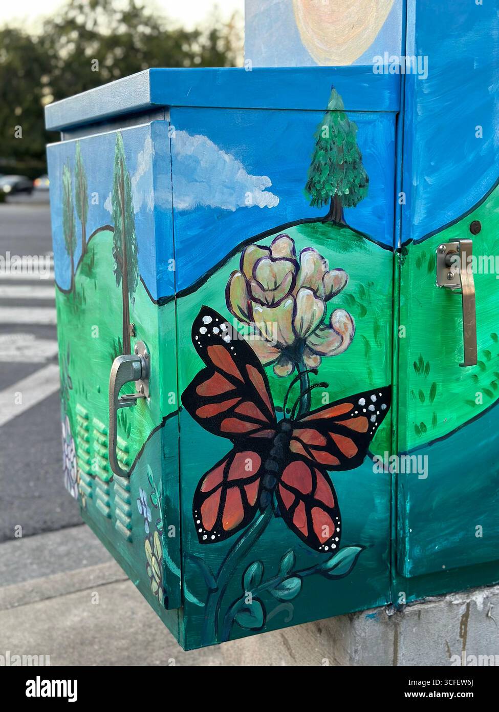 Una cassetta di servizio dipinta con colori vivaci che presenta una farfalla monarchica, fiori, colline verdi e cieli blu, catturati in un angolo di strada. - Immagine stock catturata con smartphone