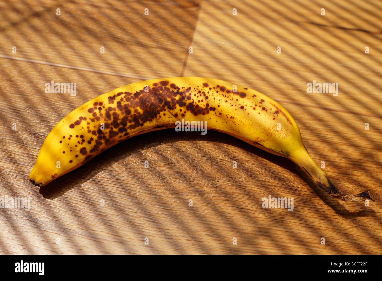 Banana che poggia su pavimento in legno con motivi ombra durante la luce del giorno Foto Stock