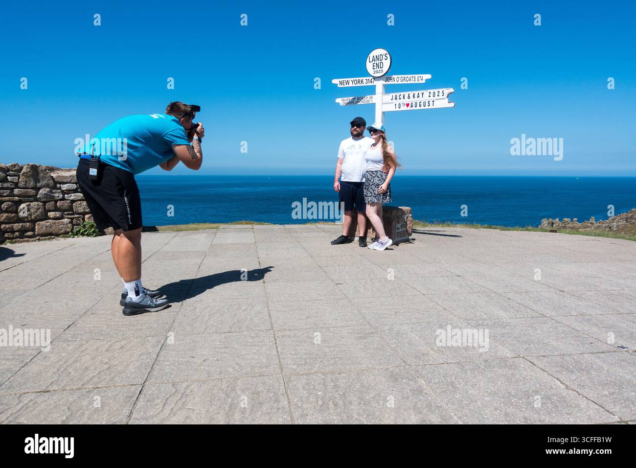 Coppia fotografata al cartello Land's End in Cornovaglia, Inghilterra, Regno Unito Foto Stock