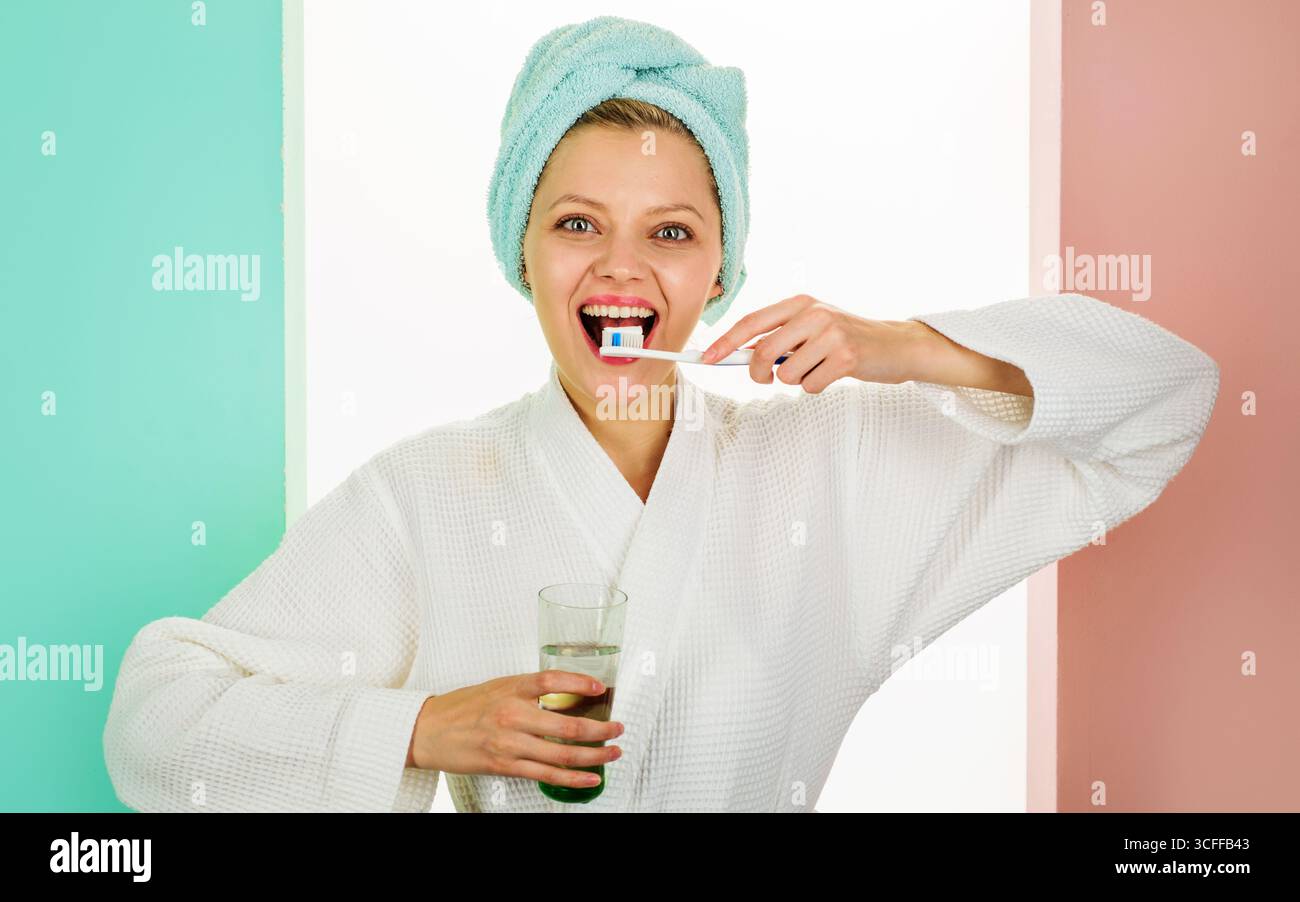 Cure dentistiche. Donna felice in accappatoio con acqua di vetro e spazzolino da denti. Igiene orale. Ragazza sorridente che pulisce i denti con lo spazzolino e il dentifricio Foto Stock