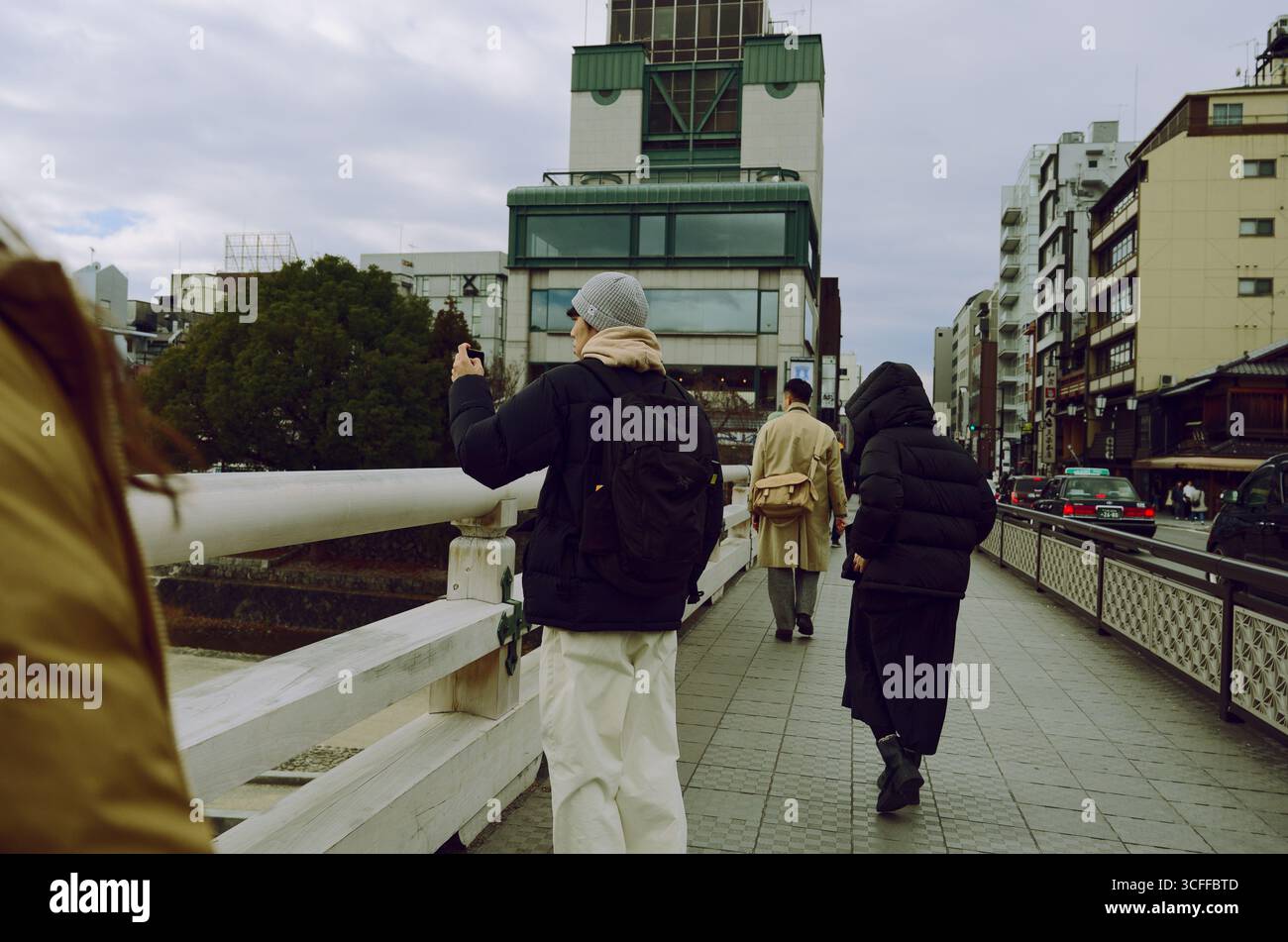 I pedoni attraversano un ponte di Kyoto in una giornata nuvolosa, una sosta per scattare una foto mentre il traffico e gli edifici incorniciano la scena Foto Stock