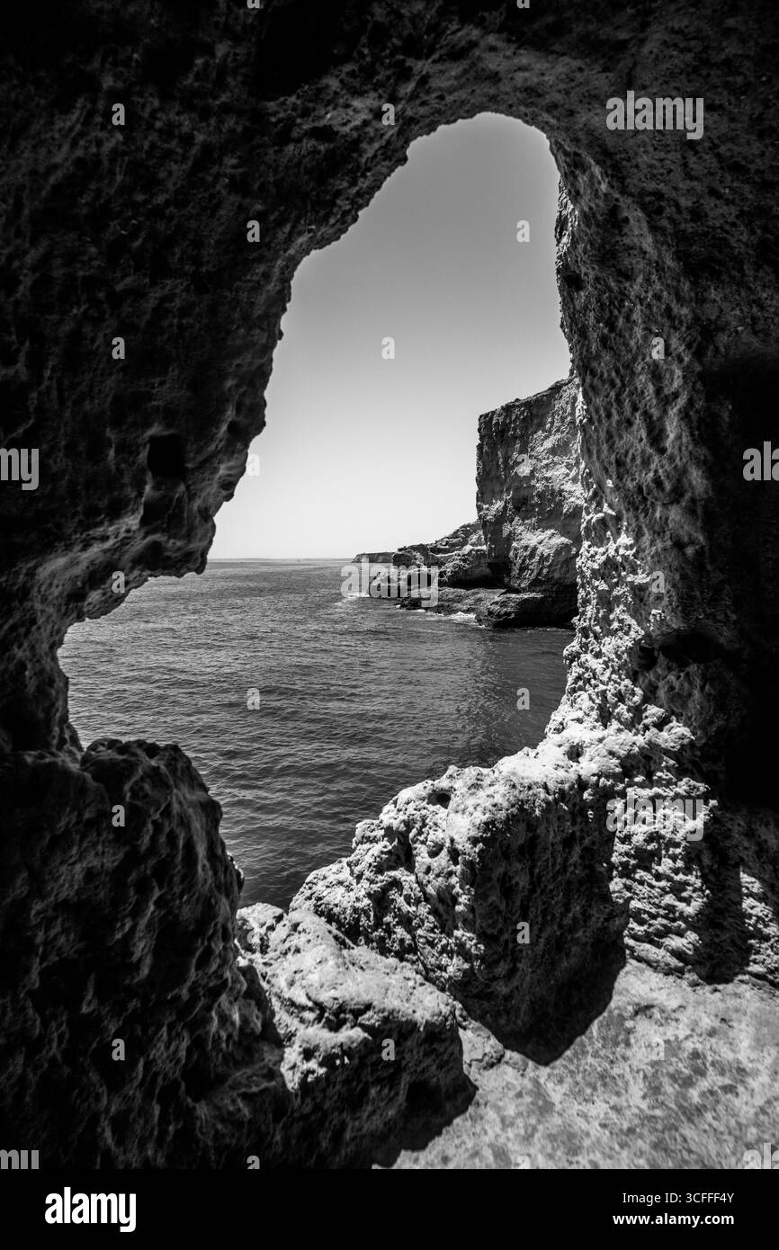 Algarve, Portogallo – 2025.06.30 – Vista panoramica delle acque turchesi dell'Atlantico e delle aspre scogliere incorniciate da una grotta di roccia naturale che si apre lungo l'Algarve co Foto Stock