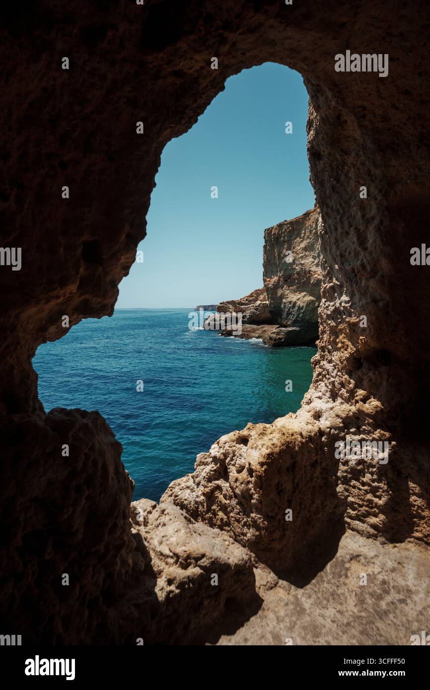 Algarve, Portogallo – 2025.06.30 – Vista panoramica delle acque turchesi dell'Atlantico e delle aspre scogliere incorniciate da una grotta di roccia naturale che si apre lungo l'Algarve co Foto Stock