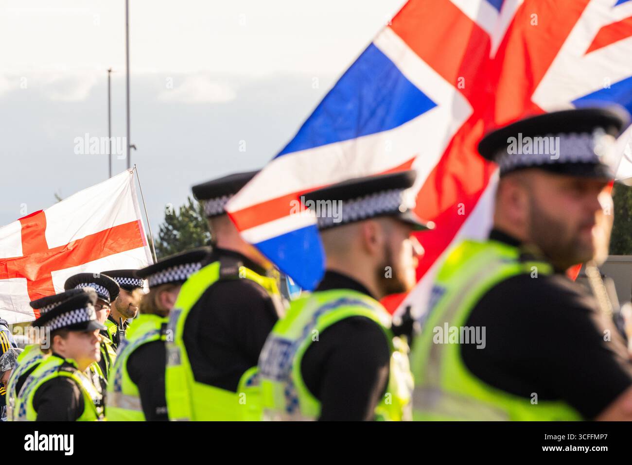 Leeds, Regno Unito. 22 AGOSTO 2025. La polizia osserva i manifestanti anti anti-migranti riuniti con le bandiere fuori dal Britannia Hotel a Seacroft, Leeds, per il quinto venerdì consecutivo. Un uomo è stato arrestato per aggressione comune dopo aver interferito con i manifestanti contro-migranti riuniti. Credito Milo Chandler/Alamy Live News Foto Stock