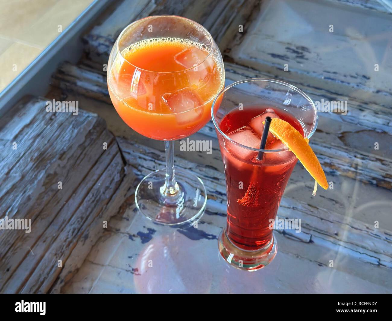 Due cocktail colorati con ghiaccio e arancia serviti su un tavolo rustico in legno alla luce dell'estate. Foto Stock