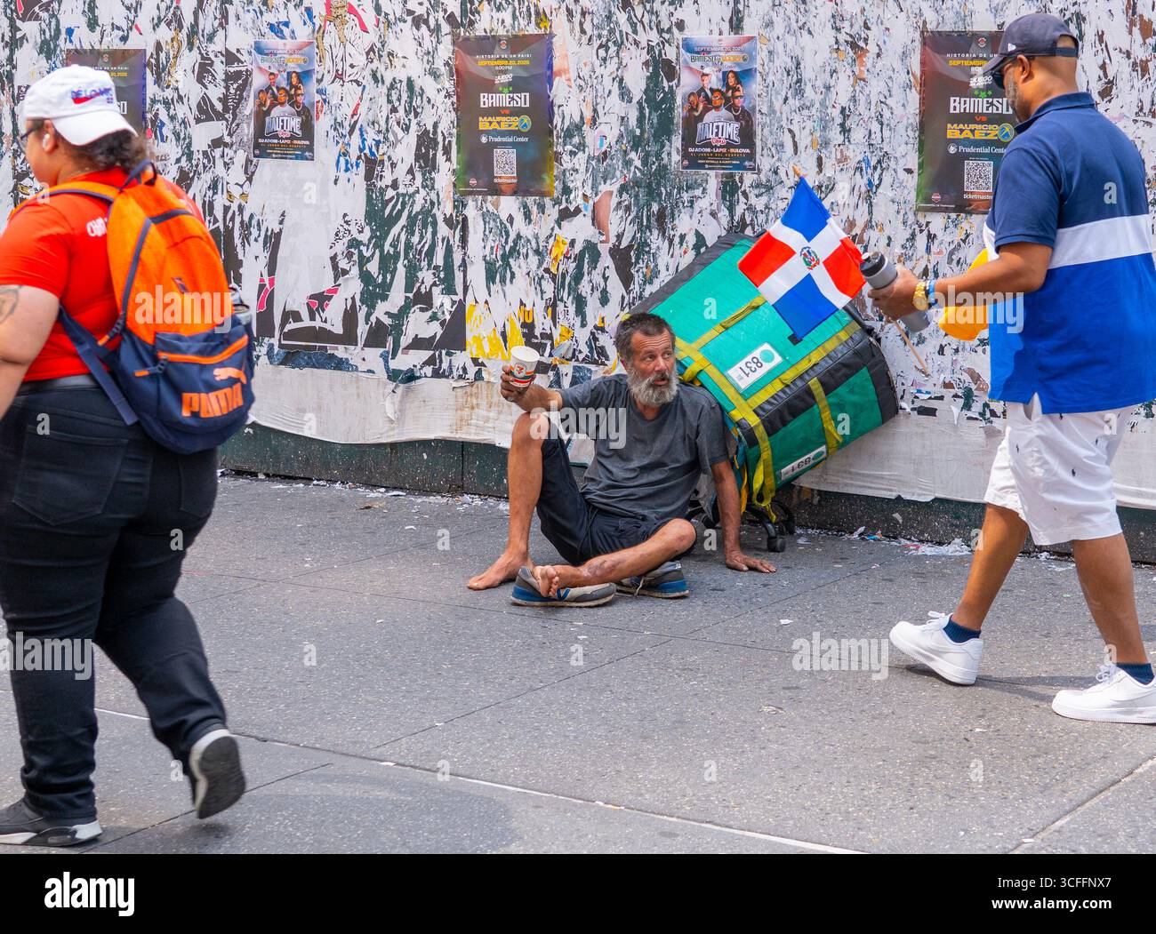 Le persone che partecipano alla National Dominican Day Parade passano accanto a un senzatetto che chiede aiuto lungo la 6th Avenue a New York City. Foto Stock
